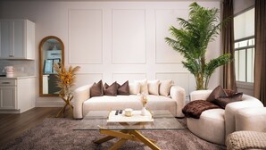 Una sala de estar moderna con un sofá color beige, una mesa de centro de cristal y una planta verde grande.