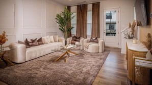 Una sala de estar moderna con un sofá color beige, una mesa de centro de vidrio y una planta grande.