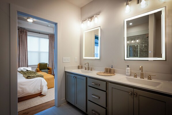 A modern bathroom with dual sinks, a large mirror, and a bed in the adjacent room. - Opulent Haven ~ Luxury Retreat in the heart of Atlanta (Atlanta)