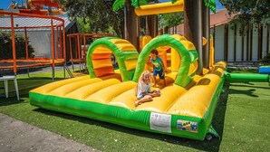 An inflatable play structure with slides and tunnels, surrounded by a fenced area with artificial grass.