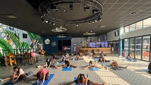 Un vaste espace intérieur doté d’un plafond haut, de nombreux tapis de yoga disposés sur le sol et d’une scène équipée d’un système d’éclairage.