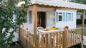 A small, single-story mobile home with a wooden deck and a covered patio area. - ZEcamping espace aquatique animaux acceptés club enfant locatif 4 pers (Saint-Hilaire-de-Riez)