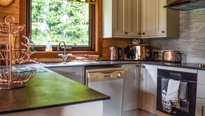 Una cocina con encimera verde, armarios blancos, lavavajillas, estufa y ventana con vistas al verdor.