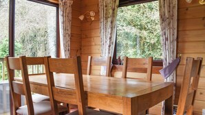 Una mesa de madera para comer con seis sillas, rodeada de amplios ventanales con cortinas florales.