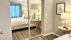 A bedroom with a bed, a bedside table with a lamp, a mirror, and a framed picture on the wall. - Your Little Guest House (Kennewick)