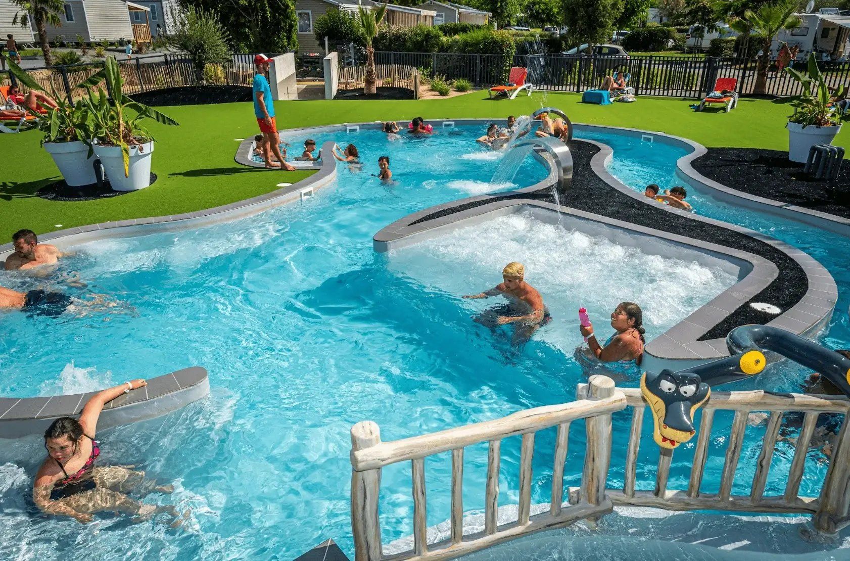 Une piscine dotée de plusieurs couloirs, entourée d’une terrasse en bois et d’une zone herbeuse.