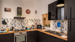 Une cuisine moderne avec des meubles de couleur sombre, un plan de travail en bois, un four encastré, un four à micro-ondes et un évier. Le mur derrière l’évier est décoré de carreaux et quelques plantes en pot y sont disposées.