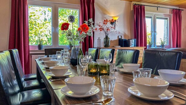 A dining area with a long wooden table set for a meal, surrounded by leather chairs.