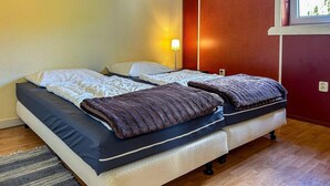 A double bed with a dark blue mattress and a brown blanket, a bedside table with a lamp, and a window with a view of greenery.