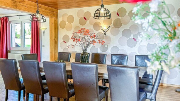 Ein Essbereich mit Holztisch und Stühlen, einer Blumenvase und einer Wand mit kreisförmigen Mustern.