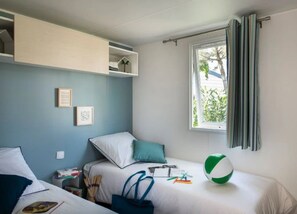 A bedroom with a bed, a window with curtains, a shelf with books, and a beach ball.