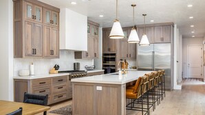 A modern kitchen with wooden cabinets, a central island, bar stools, and pendant lighting.