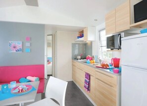 Een moderne keuken met een eethoek, met een witte koelkast, houten kastjes en een eettafel met kleurrijke stoelen.