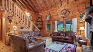 A wooden cabin interior with a staircase, leather sofas, a fireplace, and a large window. - Views for Days-Big Game Room-Hot Tub-3 King Beds! (Blue Ridge)