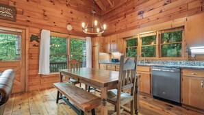 A wooden cabin interior with a dining table, benches, a chandelier, wooden cabinets, and a kitchen area. - Views for Days-Big Game Room-Hot Tub-3 King Beds! (Blue Ridge)