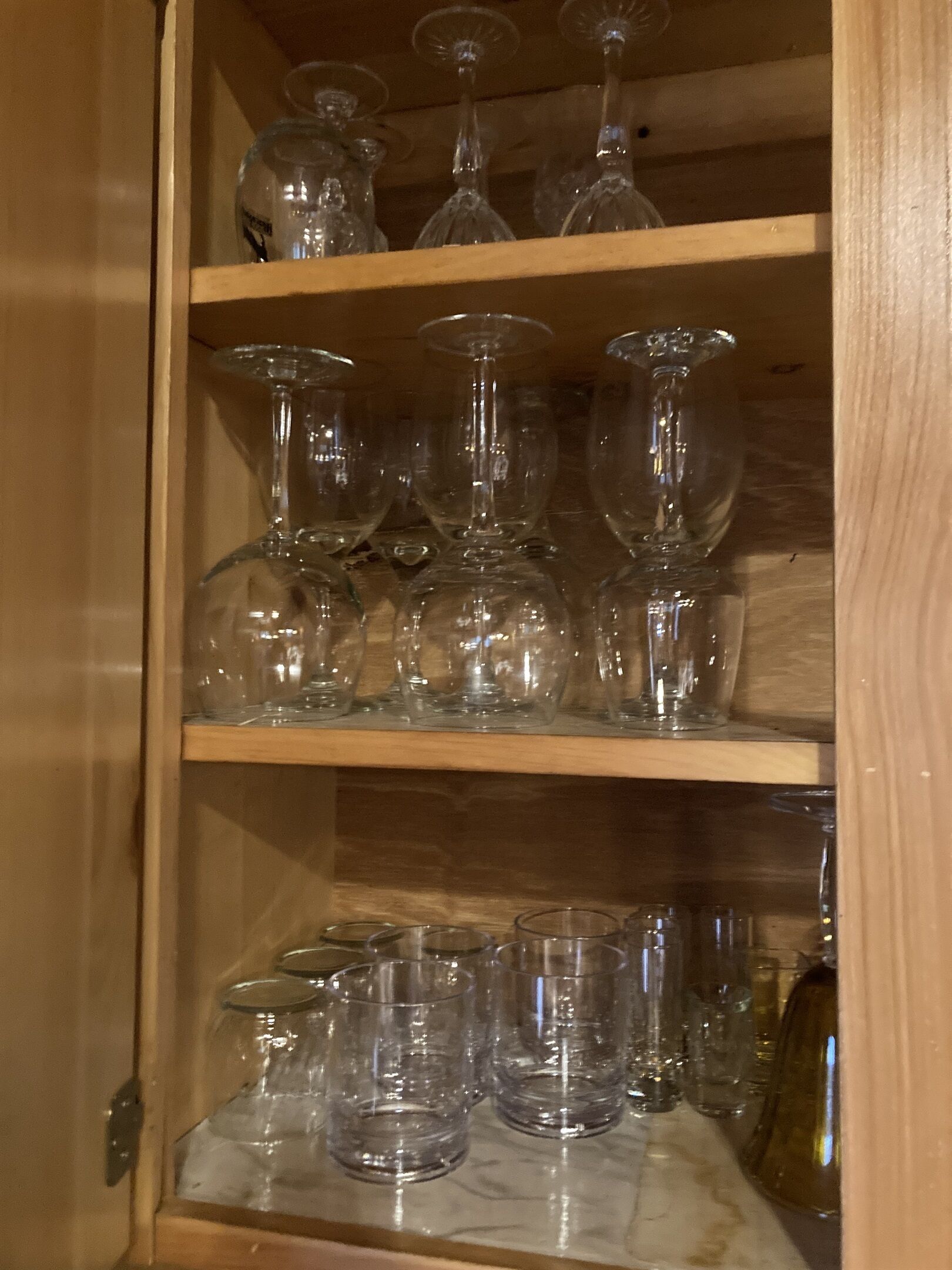 Un mobiletto in legno con diversi ripiani che espongono vari bicchieri, tra cui calici da vino e bicchieri tumbler.