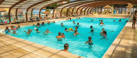 An indoor swimming pool with a curved roof structure, surrounded by tiled flooring.