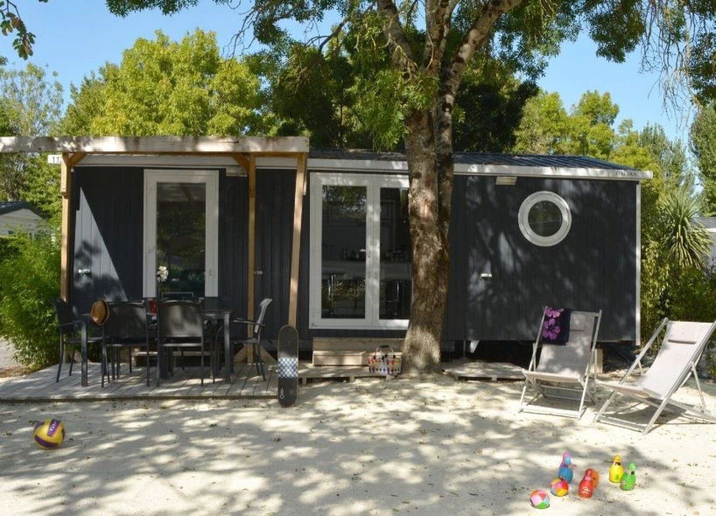 Een stacaravan met terras, buitenmeubels en een boom op de achtergrond.