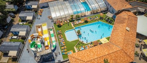 An aerial view of a resort with a large swimming pool, a water slide, and several lounge areas.