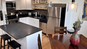 A modern kitchen with white cabinets, stainless steel appliances, a central island, and a dining area with a wooden table and chairs. - Charming 2-bedroom house with AC, WiFi in the Sky Valley Country Club. (Dillard)