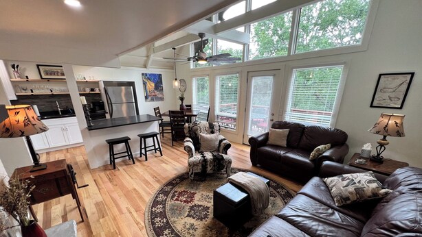 A modern living room with a brown leather sofa, a dining area with a black table, and a kitchen with white cabinets. - Charming 2-bedroom house with AC, WiFi in the Sky Valley Country Club. (Dillard)