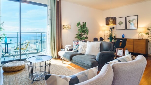 A modern living room with a sofa, armchairs, a coffee table, and a balcony with a view. - GuestReady - Fantastic home near the beach (Funchal)