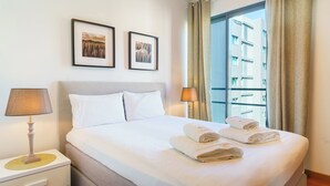 A hotel room with a bed, two framed pictures on the wall, a nightstand with a lamp, and a window with curtains. - GuestReady - Fantastic home near the beach (Funchal)