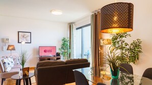 A modern living room with a sofa, a glass dining table, and a TV displaying "GUEST READY". - GuestReady - Fantastic home near the beach (Funchal)