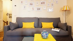 A living room with a grey sofa, yellow cushions, a vase, and framed pictures on the wall. - Coppelle Charme - Three Bedroom Apartment, Sleeps 6 (Rome)