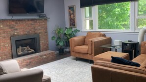A living room with a fireplace, a sofa, a TV, and a skylight. - A beautiful 4 BDR home, newly renovated and close to everything! (Williston)