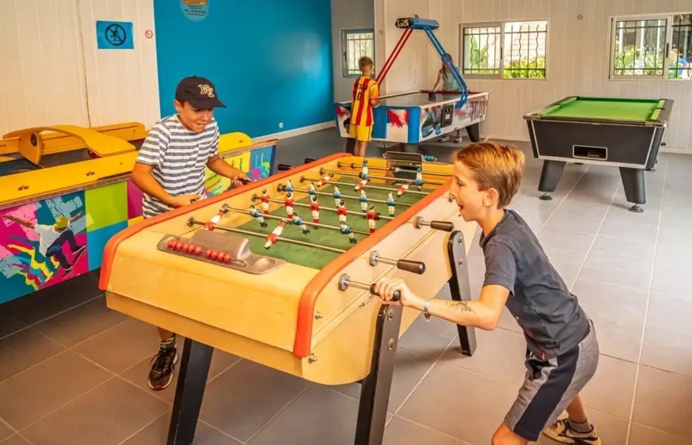 Una habitación con mesa de fútbol, mesa de billar y un mural de colores en la pared.