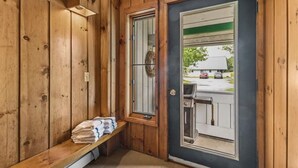 Un cuarto de sauna con paredes de madera, un banco con toallas y una puerta que da al exterior.