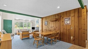 Una habitación con una mesa de comedor de madera, sillas, una pizarra verde y una ventana con vista a árboles.