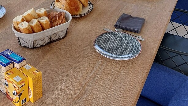 Et morgenbord dækket med brød, kager og frugt, med udsigt til grønne omgivelser.