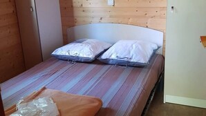 Uma cama de solteiro com cabeceira, parede de madeira e uma mesinha com uma mala em cima.