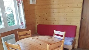 A wooden dining table with four chairs, a bench, and a window with curtains. - Chalet 4 étoiles - ccaiaag (Monoblet)