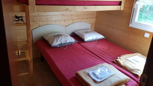A bunk bed with a red mattress, pillows, and a wooden ladder. - Chalet 4 étoiles - ccaiaag (Monoblet)
