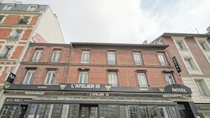A building with a 'HOTEL' sign and 'L'ATELIER 15' sign above the entrance. - Hôtel Trianon Saint Ouen (Saint-Ouen)