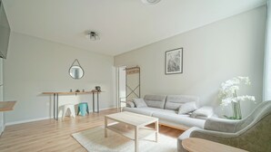 A modern living room with a sofa, a coffee table, and a side table. There is a mirror on the wall and a framed picture above the sofa. - Hôtel Trianon Saint Ouen (Saint-Ouen)
