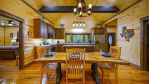 Interior de una cabaña de madera con comedor, cocina y un ventanal grande.