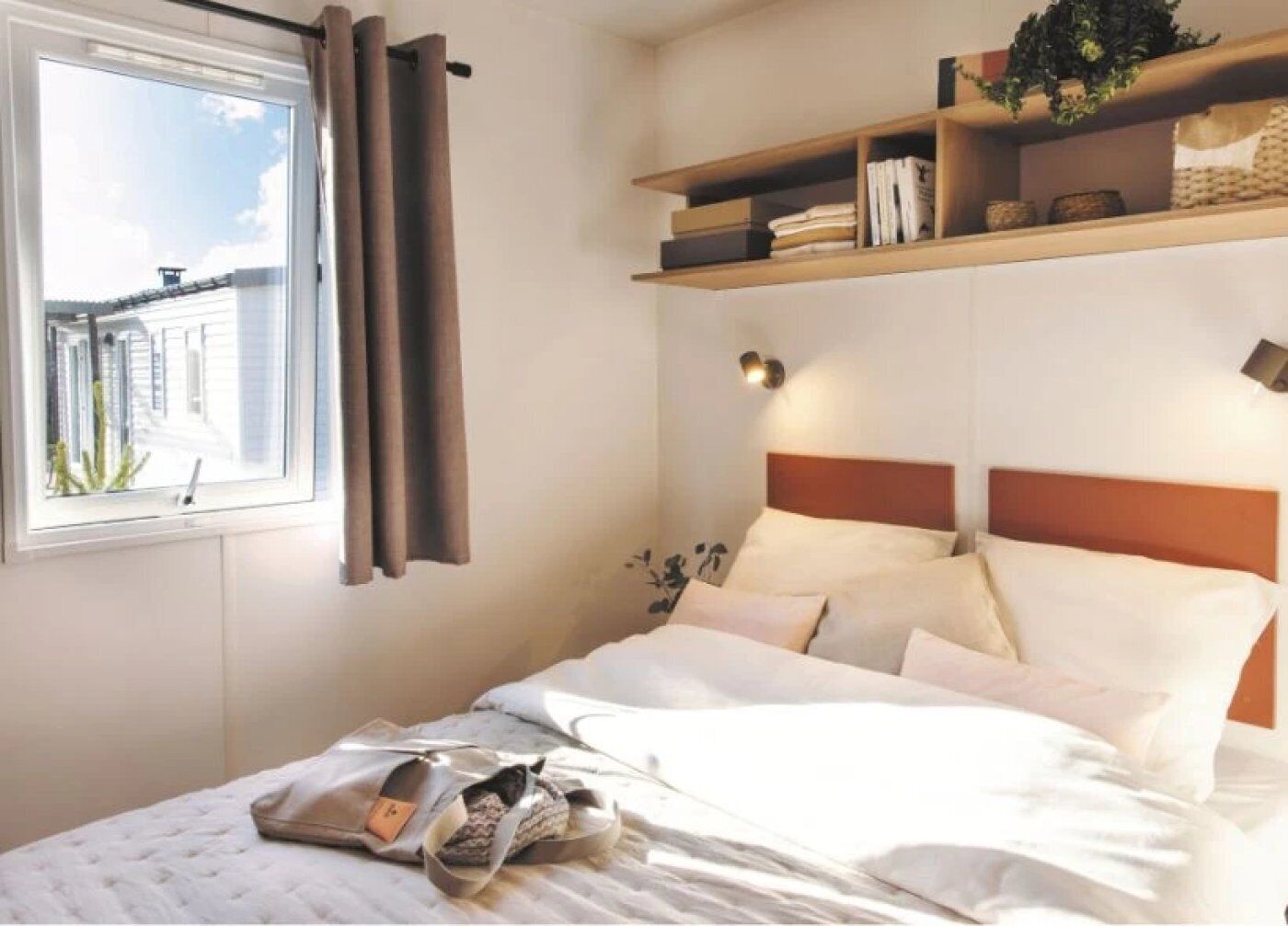 Un lit avec une tête de lit, une table de chevet, une étagère avec des livres et une fenêtre avec des rideaux.