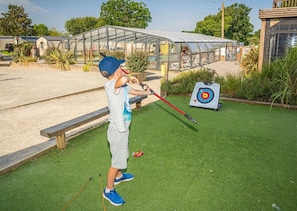 A child playing with a slingshot in a grassy area with a target in the background.