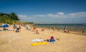 A beach with people sunbathing and swimming, tents, and a clear sky.