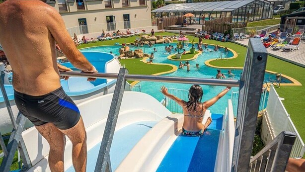 Un tobogán de agua en un área de piscina con varias piscinas y sillas de descanso.