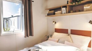 A bed with a headboard, a bedside table, a shelf with books, and a window with curtains.