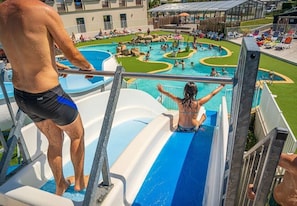 Un tobogán de agua en un área de piscina con varias piscinas y sillas de descanso.
