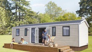A single-story mobile home with a deck, a covered patio, and a small outdoor seating area.