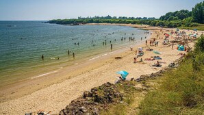 A beach with people swimming and sunbathing, a rocky shoreline, and a clear view of the sea.