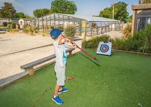 A child playing with a slingshot in an outdoor area with a target and a transparent structure in the background.