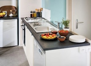 A modern kitchen with a black countertop, a gas stove, and various kitchen utensils. There are bowls of fruit and a white cabinet.